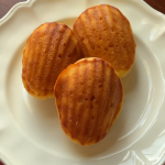 Photo of three cornbread madeleines on a white plate with a wooden table in the background